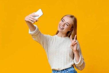 Gülümseyen genç kız akıllı telefondan selfie çekiyor, barış jesti gösteriyor.