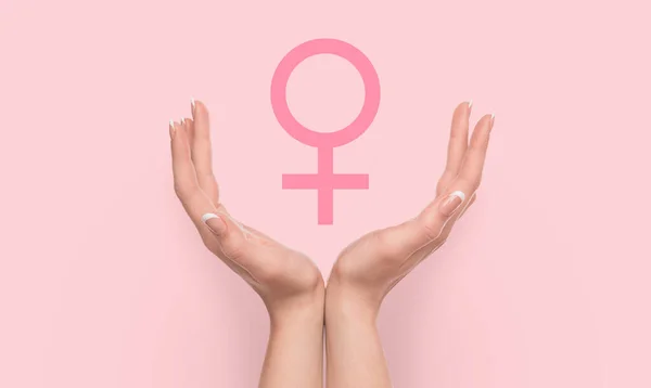 Manos de mujer sosteniendo signo de género femenino sobre fondo rosa . — Foto de Stock