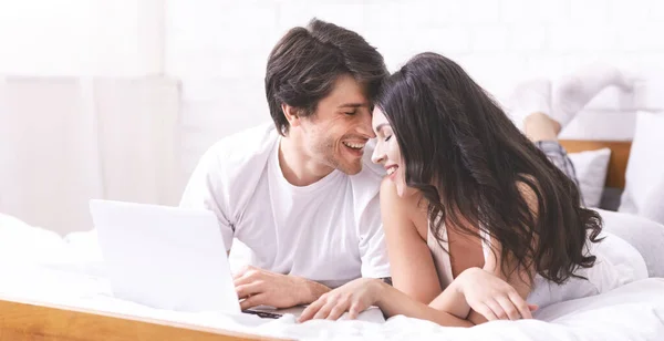 Joven hombre y mujer navegando en el ordenador portátil en la cama — Foto de Stock