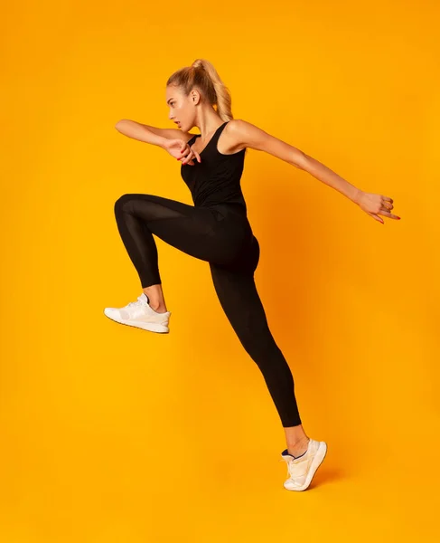 Jonge dame springen tijdens de training op gele achtergrond, zijaanzicht — Stockfoto