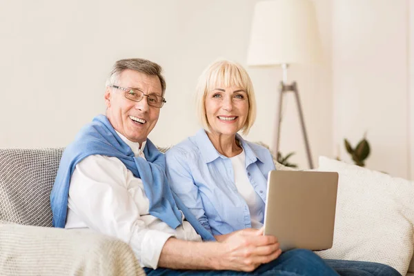 Radostný starší pár s notebookem s úsměvem na kameru — Stock fotografie