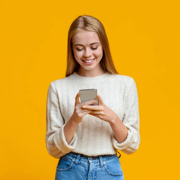 Όμορφο κορίτσι Μηνύματα σε Smartphone πάνω από πορτοκαλί φόντο — Φωτογραφία Αρχείου