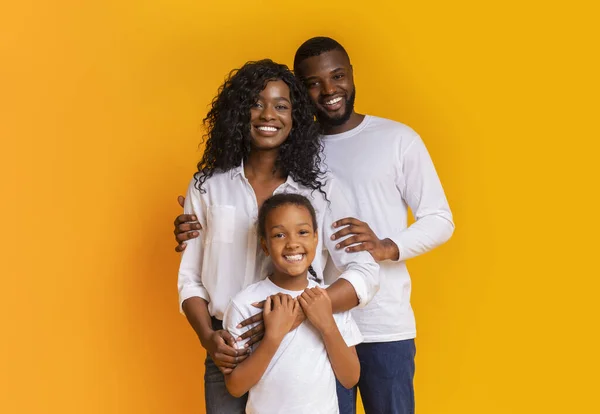 Família feliz de três abraços e posando sobre fundo amarelo — Fotografia de Stock