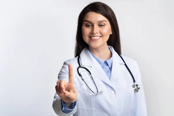 Doctor vrouw aanraken onzichtbare touchscreen staande over grijze achtergrond — Stockfoto