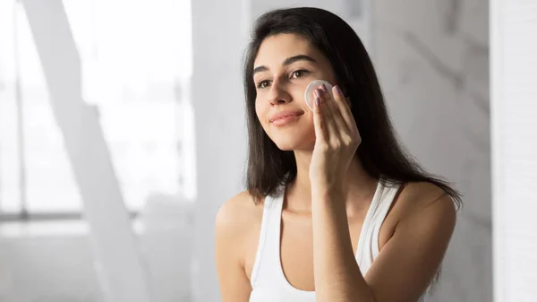 Jovem mulher removendo maquiagem usando almofada de algodão no banheiro — Fotografia de Stock