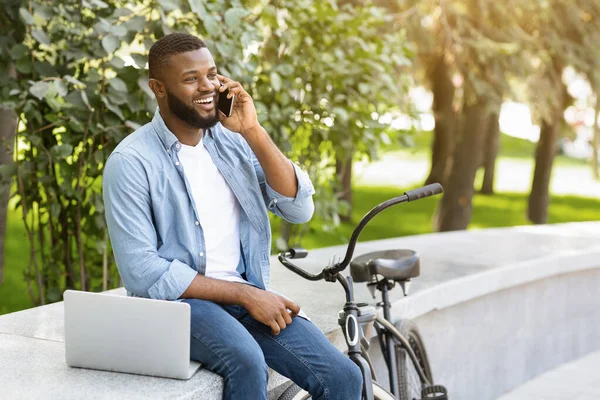 Cara falando no telefone, sentado ao ar livre com laptop e bicicleta — Fotografia de Stock