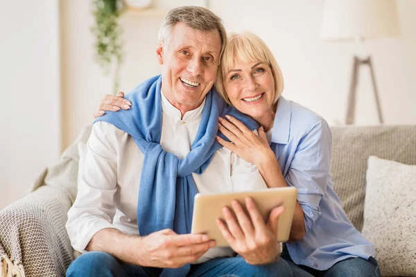 Excited mature couple with digital tablet smiling to camera — 스톡 사진