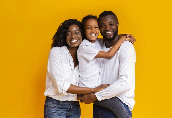 Pais felizes e filha abraçando uns aos outros sobre fundo amarelo — Fotografia de Stock