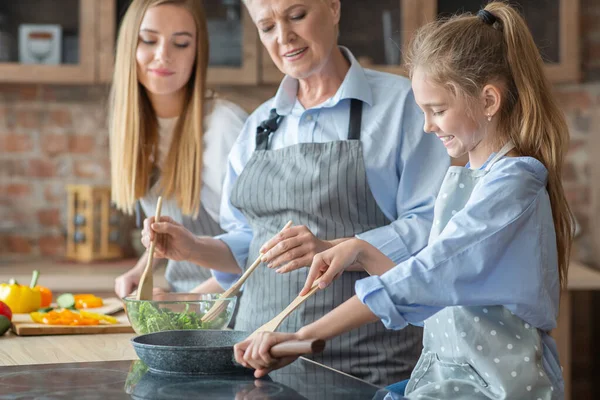 Χαμογελώντας κορίτσι τηγάνισμα λαχανικών, βοηθώντας τη μαμά και τη γιαγιά στην κουζίνα — Φωτογραφία Αρχείου