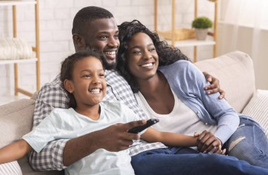 Üç kişilik Afro-Amerikan Ailesi Kanepede oturmuş televizyon izliyor.