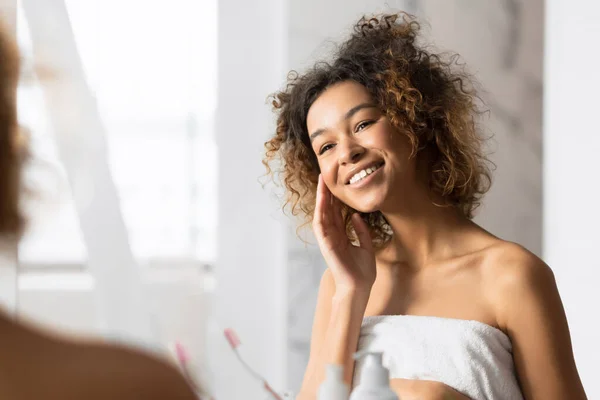 Chica tocando la cara con la piel perfecta mirando en el espejo del baño —  Fotos de Stock