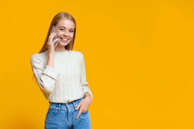 Portakal rengi stüdyoda telefonla konuşan güzel bir genç kadın.