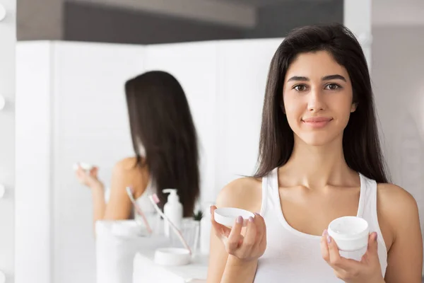 Jonge vrouw Holding gezichtscrème product staande in de badkamer — Stockfoto