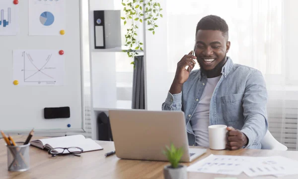 Fröhlicher schwarzer Manager, der am Handy telefoniert und Kaffee trinkt — Stockfoto