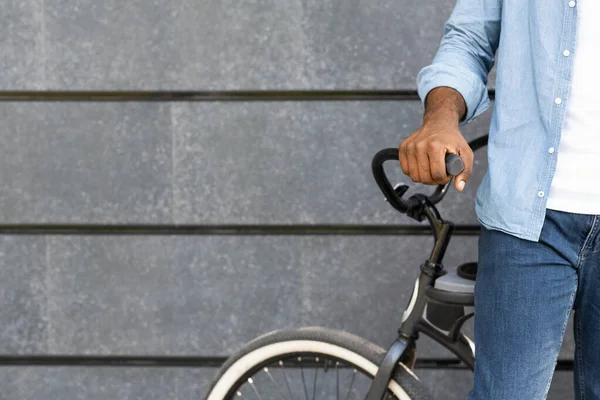 Hombre negro irreconocible de pie cerca de la bicicleta contra fondo gris de la pared — Foto de Stock