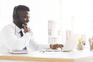 Kulaklıklı neşeli bir çalışan dizüstü bilgisayarın önünde oturuyor.