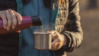 Kadın termostan bardağa sıcak su dolduruyor.