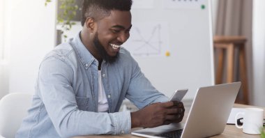 Akıllı telefon ekranına bakan mutlu siyah yönetici hoş bir mesaj okuyor