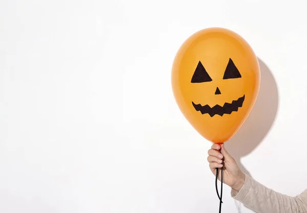 Halloween orange balloon with smiling face in woman hand