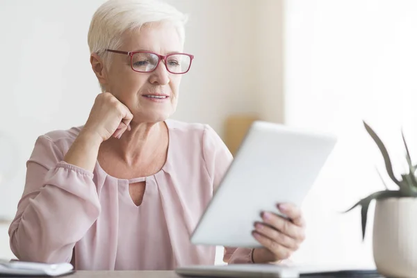 Lächelnde Seniorin mit Brille liest Buch auf digitalem Tablet — Stockfoto