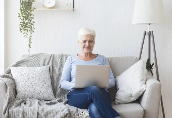 Ambitna starsza pani korzystająca z laptopa na sofie w domu — Zdjęcie stockowe