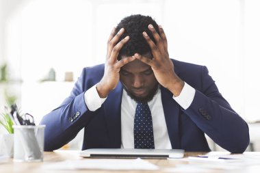 Stresli iş adamı ofiste oturuyor ve eli alnında.
