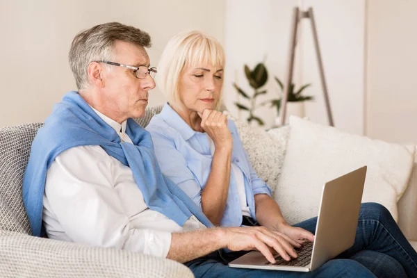 Vážné starší pár websurfing, čtení novinek na notebooku — Stock fotografie