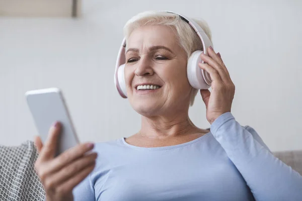 Seniorin mit Headset genießt Musik, schaut Videos auf Smartphone — Stockfoto