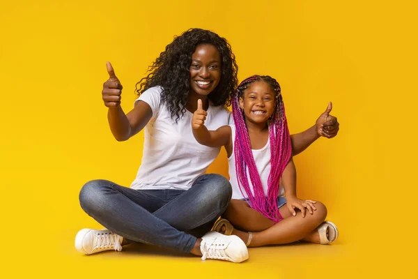 Moeder en dochter krijgen duimen omhoog over gele achtergrond. — Stockfoto