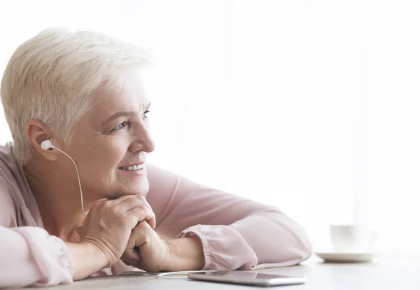 Porträt einer verträumten alten Dame, die am Telefon Musik hört — Stockfoto