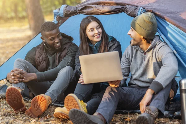 Trois amis heureux assis dans la tente de camping et en utilisant un ordinateur portable — Photo