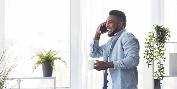 Mladý veselý podnikatel mluví po telefonu a drží šálek kávy — Stock fotografie