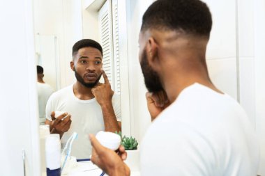 Yakışıklı Afrikalı adam banyoya nemlendirici krem sürüyor.