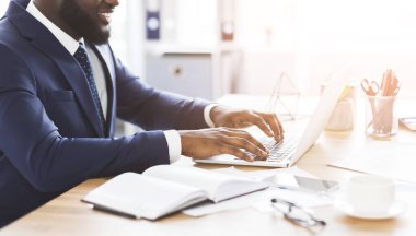 Dizüstü bilgisayarda yazan takım elbiseli Afrikalı bir adam.