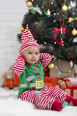 Noel kostümüyle Noel ağacının altında oturan tatlı bebek.