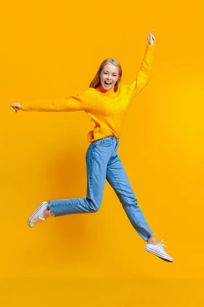 Springen millennial meisje in de lucht over oranje studio achtergrond — Stockfoto