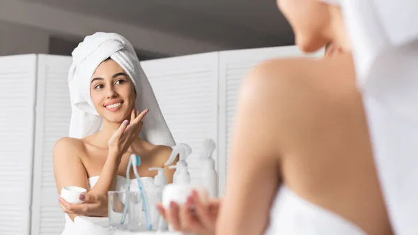 Sorrindo Millennial menina aplicando creme facial hidratante pele no banheiro — Fotografia de Stock