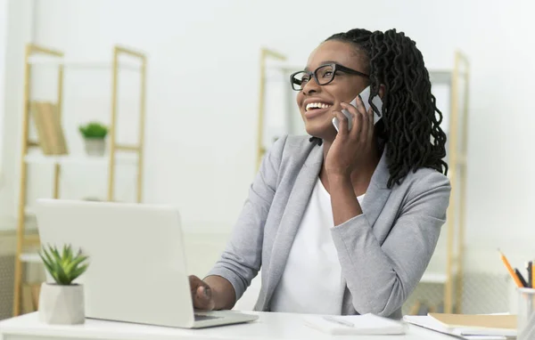 Черный предприниматель леди разговаривает по мобильному телефону, сидя в современном офисе — стоковое фото