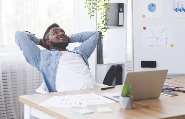 Dreamy black employee resting at workplace with hands behind head