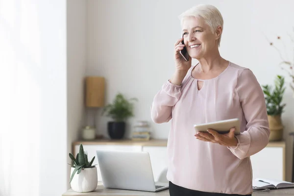 Drukke oude vrouw consultancy client via de telefoon, met behulp van tablet — Stockfoto