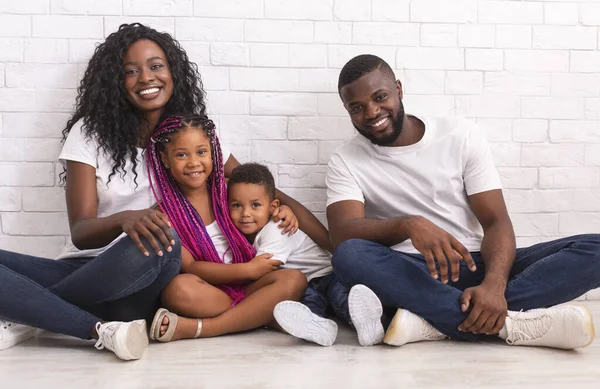 Moeder, vader en twee kinderen zitten op de vloer en knuffelen — Stockfoto