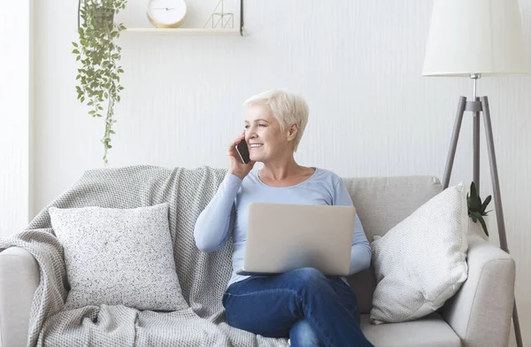 Moderne alte Dame hält Laptop in der Hand und telefoniert — Stockfoto