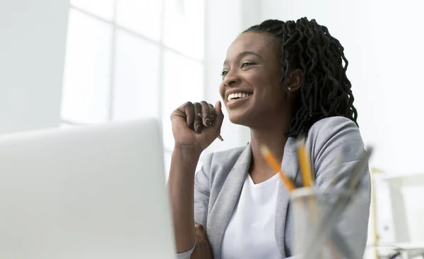 La señora de los negocios sonriendo sentada en el ordenador portátil contra la ventana en la oficina — Foto de Stock