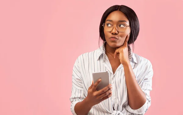 African American Girl Using Smartphone and Thinking Over Pink Background — стоковое фото