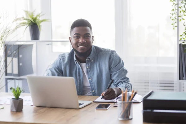 Portret van een lachende zwarte stagiair die aantekeningen maakt op een nieuwe werkplek — Stockfoto