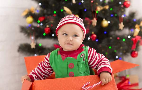 Bebê curioso procurando presentes de Natal em caixa grande sob árvore de Natal — Fotografia de Stock