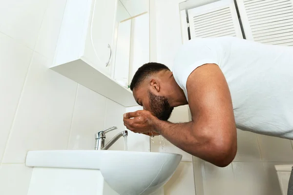 African man washing his face in bathroom