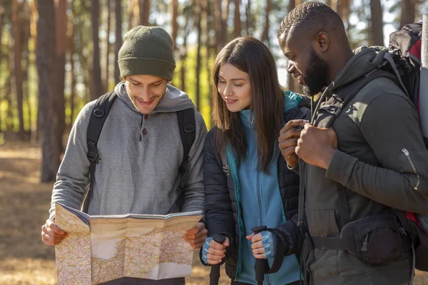 Vidám barátok hátizsákokkal nézi a térképet az erdőben — Stock Fotó