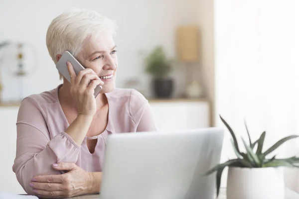 Positieve oude vrouw praten via de telefoon met klanten — Stockfoto