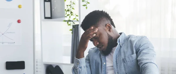 Przepracowany czarny biznesmen cierpiący na ból głowy w miejscu pracy w biurze — Zdjęcie stockowe